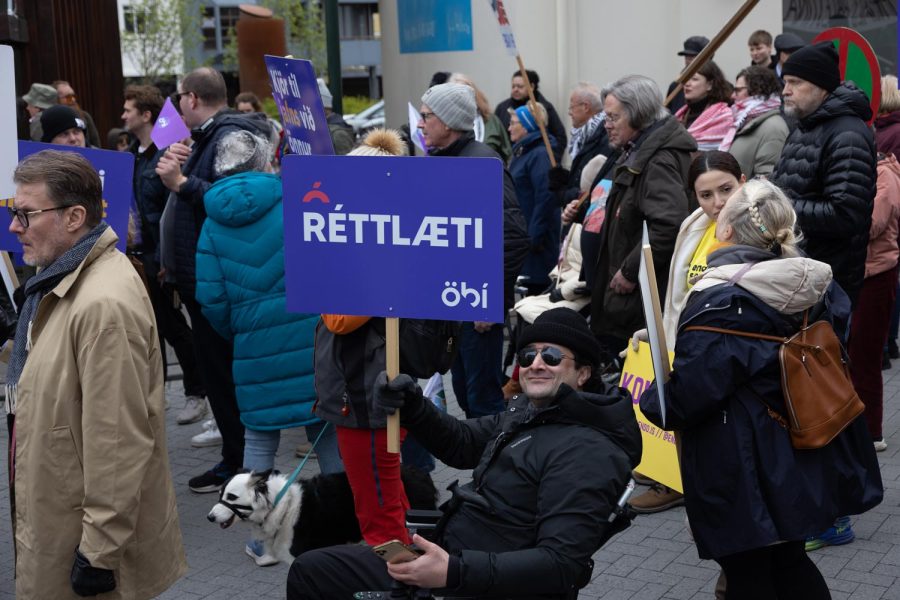 Á myndinni er hópur fólks á Ingólfstorgi á 1. maí 2025. Flest eru í hlýjum vetrarfötum og margir bera skilti. Í forgrunni situr brosandi karlmaður í hjólastól, klæddur dökkum fatnaði og með sólgleraugu. Hann heldur á fjólubláu skilti sem á stendur „RÉTTLÆTI“ ásamt merki ÖBÍ réttindasamtaka. Í kringum hann er fleira fólk. Sumir með kröfuskilti og sumir að tala saman eða fylgjast með. Stemningin á myndinni virðist samheldin og baráttuglöð, þar sem fjölbreyttur hópur fólks tekur þátt.