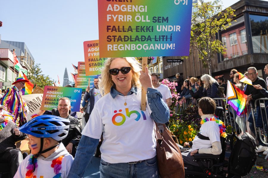 Hópur fólks úr ÖBÍ réttindasamtökum tekur þátt í Gleðigöngunni fyrir framan Hallgrímskirkju. Þau bera skilti með textanum „Skert aðgengi fyrir öll sem falla ekki undir staðlaða liti regnbogans!“ Formaður ÖBÍ, Alma Ýr Ingólfsdóttir fremst í broddi fylkningar ásamt syni sínum.