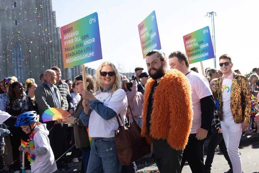 Hópur fólks úr ÖBÍ réttindasamtökum tekur þátt í Gleðigöngunni fyrir framan Hallgrímskirkju. Þau bera skilti með textanum „Skert aðgengi fyrir öll sem falla ekki undir staðlaða liti regnbogans!“ Fremst í broddi fylkningar er formaður ÖBÍ, Alma Ýr og Þórgnýr Einar upplýsingafulltrúi ÖBÍ.