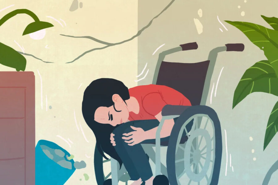 Teiknuð mynd af konu í hjólastól sem hefur tekið felustellingu með höfuð á hnénu og hendur um fætur. Í kringum hana sjást sprungur í veggjum, fötu með vatni sem hefur dottið um koll og plöntur sem halla, sem gefur til kynna að jarðskjálfti sé í gangi.