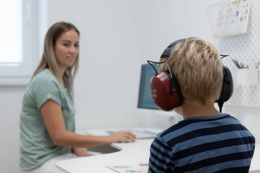 Mynd: „Barn situr við borð með heyrnartól í heyrnarmælingu, sérfræðingur fylgist með.“