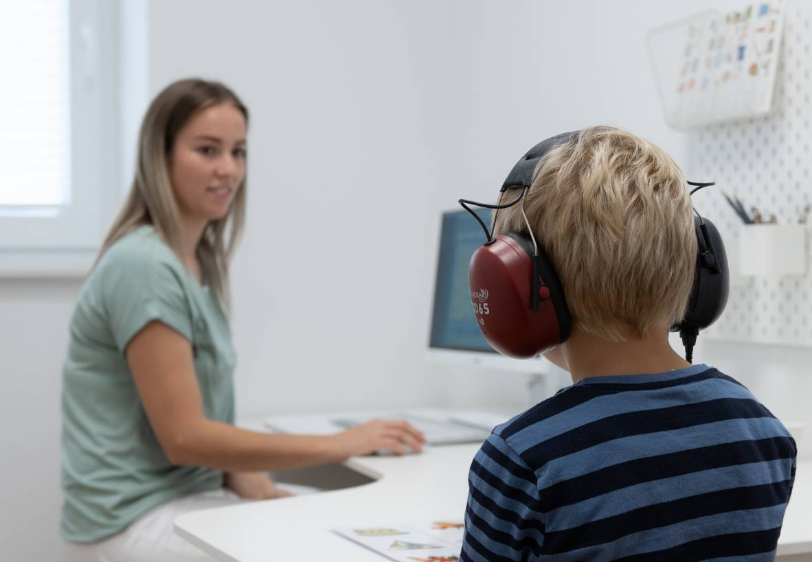 Mynd: „Barn situr við borð með heyrnartól í heyrnarmælingu, sérfræðingur fylgist með.“