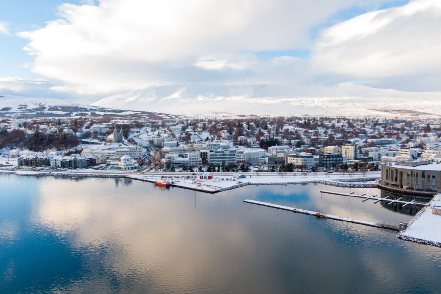 Yfirlitsmynd af Akureyri. Snjór yfir bænum og skýin speglast á sjónum.